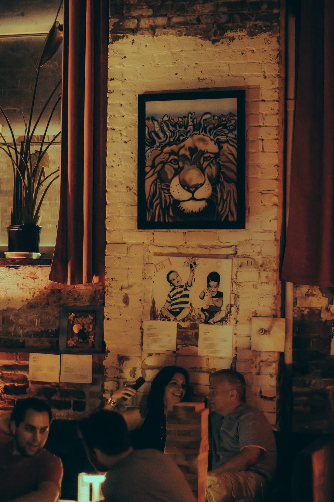 A wall of framed artwork above plants, lit amber